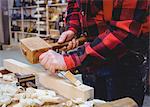 Carpenter working on a wooden plan with an hammer in his workplace