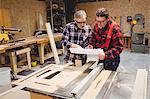 Duo of carpenters studying plans in workshop