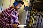 Technician in head phones using digital tablet while analyzing server in server room