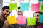 Happy creative business people writing on sticky notes seen through glass in office