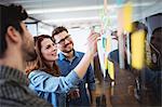 Businesswoman writing on sticky notes as coworkers looks at her