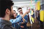 Smiling businesswoman writing on sticky notes as coworkers looks at her