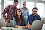 Portrait of smiling business people with laptop in meeting room at creative office