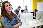 Portrait of attractive businesswoman with arms crossed standing against coworkers working in creative ofice