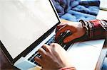 Cropped image of male customer typing on laptop at table in cafeteria