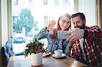 Cheerful young couple video chatting at cafe