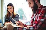 Young couple using mobile phone with coffee on table at cafe