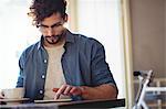 Handsome man touching smartphone while sitting with coffee at cafe