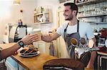 Happy young male barista serving coffee to customer at cafe