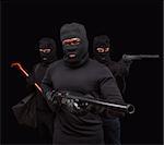 Closeup portrait of robber posing with rifle over black background with his partners. Studio shot of muscular men with weapons. Isolated on black.