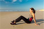 Beautiful woman sitting on the sand and relaxing after exercise
