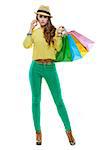 Colourful shopping vibes. Full length portrait of brunette woman in hat and bright clothes with colorful shopping bags talking smartphone on white background