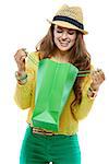 Colourful shopping vibes. Portrait of smiling brunette woman in hat and bright clothes looking inside of the green shopping bags against white background