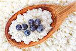 crumbly cottage cheese in the wooden spoon with blueberries on the top