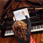 Young woman musician writes in music book pencil. Sitting in front of grand piano.