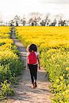 Beautiful happy mixed race African American girl teenager female young woman hiking with red recksack in yellow field in golden evening sunshine