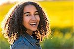 Outdoor portrait of beautiful happy mixed race African American girl teenager female young woman smiling laughing with perfect teeth in field of yellow flowers