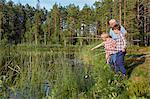 Grandfather teaching grandsons fishing at sunny lakeside