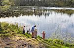 Grandfather teaching grandchildren fishing at sunny lakeside