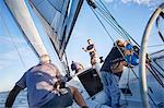 Men sailing adjusting rigging and sail on sailboat