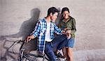 Teenage couple with BMX bicycle texting with cell phone at wall