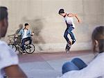Friends watching teenage boy flipping skateboard at skate park