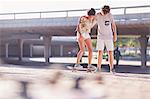 Teenage boy teaching girlfriend skateboarding at sunny skate park