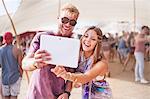 Young couple taking selfie with digital tablet at music festival