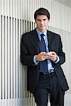 Businessman leaning against wall, using smartphone