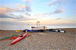 England, Suffolk, Aldeburgh. Boat and fishing paraphernalia on the shingle beach at dusk.