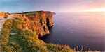 Cliffs of Moher (Aillte an Mhothair), Doolin, County Clare, Munster province, Ireland, Europe. Panoramic view with a man watching the sun setting from the top of the cliff.