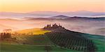 Valdorcia, Siena, Tuscany, Italy. Panoramic view of a tuscan farm on top of a hill at sunrise.