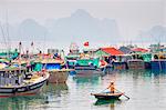 A woman in a small sampan paddles past colorful fishing boats in the harbor at Cai Rong, Quang Ninh Province, Vietnam