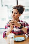 Thoughtful woman holding coffee cup while sitting at table in restaurant