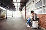 Young woman using phone while sitting at railway station
