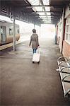 Rear view of woman carrying luggage while walking at railroad station platform