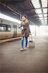 Woman carrying luggage while walking at railroad station platform