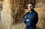 Portrait of confident farm worker standing against hay bales in barn