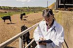 Vet writing in paper while standing by fence on sunny day