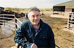 Portrait of mature farmer leaning on fence at field