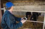 Side view of farm worker using digital tablet by fence at barn