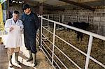 Farm worker and vet discussing over digital tablet by fence at barn