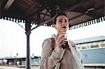 Young woman holding drink while standing at railroad station
