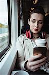 Pretty woman using mobile phone while sitting by window in train