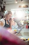 Female florist using laptop while talking on mobile phone in the flower shop