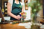 Mid section of female florist arranging flowers in a bottle at her flower shop