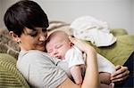 Mother holding baby while sleeping in living room at home