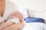 Baby with dummy sleeping in mother's arm on bed in bedroom at home