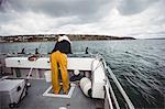 Rear view of fisherman looking into the sea from fishing boat