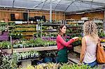 Female florist talking to woman about plants in garden centre